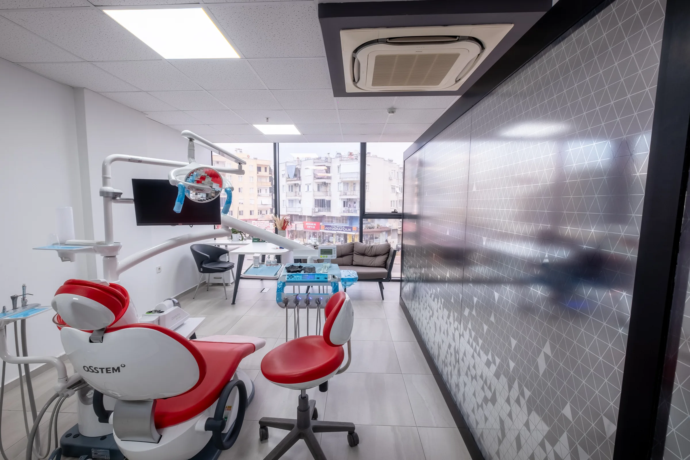 Behandelkamer met rode behandelstoel achter een glazen wand
