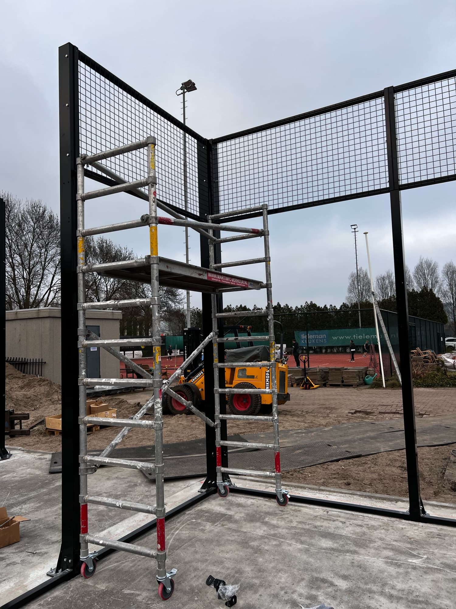 Rolsteiger tegen het hekwerk van de padelbaan tijdens montage