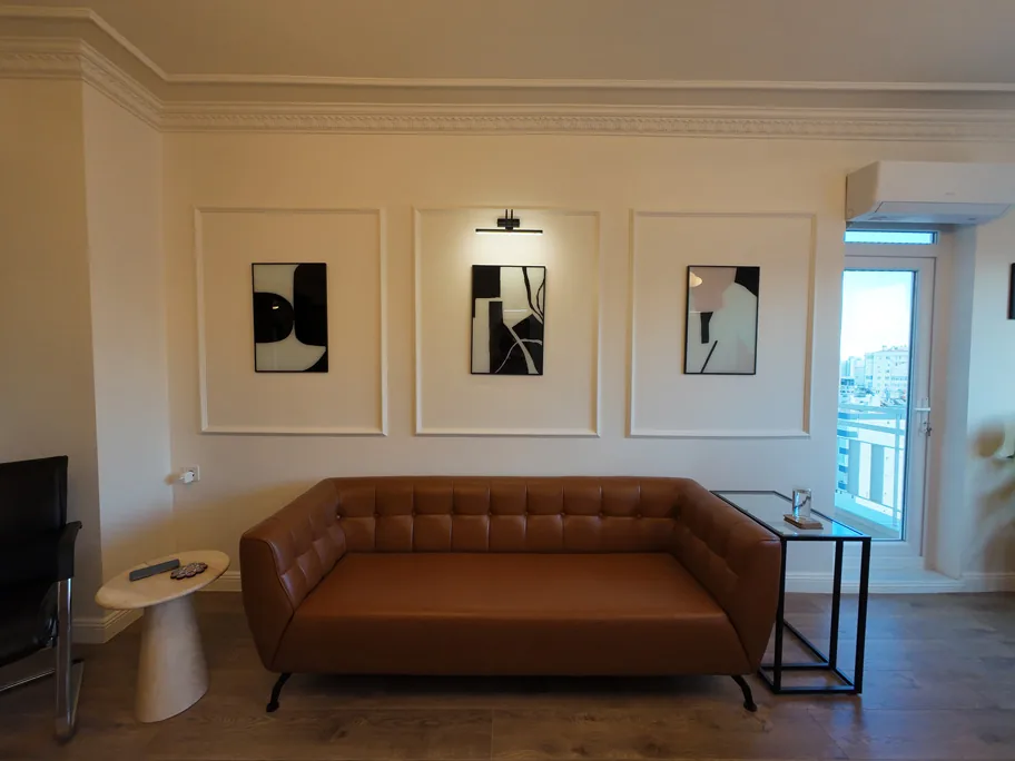 Wand met lijstwerk, ingelijste prints en leren bank